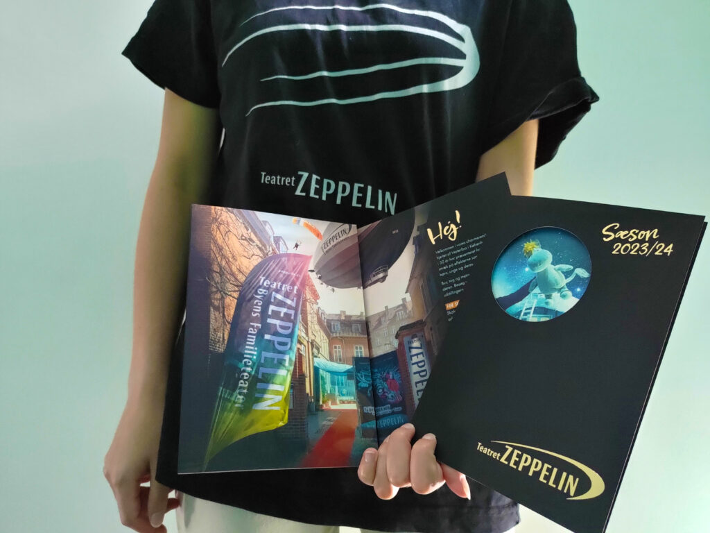 Teatret Zeppelins SoMe-medarbejder Melissa holder Teatret Zeppelins nye sæsonbrochure for 2023/24 i hånden