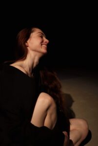 Fotografi af koreograf Anastasiia Krasnoshchoka, siddende på gulvet i et sort rum